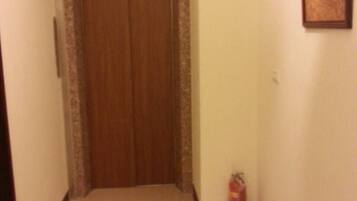 A hallway with a wooden door marked with the number 3, a fire extinguisher, and a framed picture on the wall.