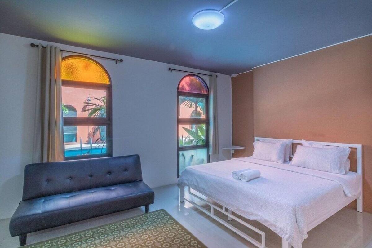 Um quarto com uma cama, um sofá e duas janelas com cortinas.