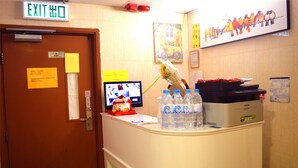 A reception desk with a computer monitor, water bottles, and a sign indicating an exit. - Mingdu Hostel (Kowloon)