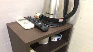 A wooden shelf with a remote control, a kettle, and a phone charger. - Mingdu Hostel (Kowloon)
