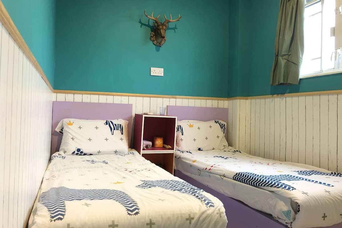 A room with two beds, teal walls, and a mounted deer head.