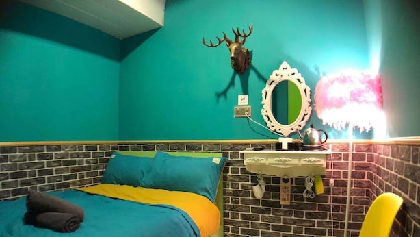 A room with a bed, a yellow chair, a mirror, and a wall-mounted deer head. - Mingdu Hostel (Kowloon)