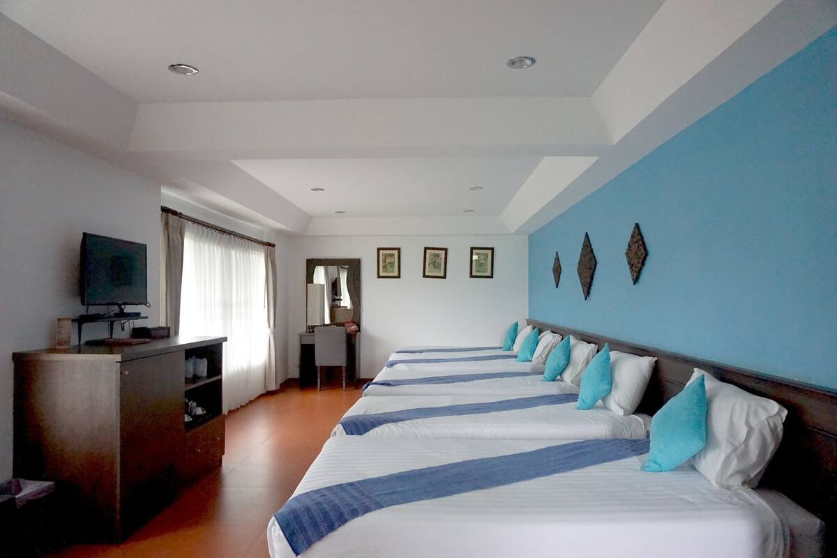 Ein Hotelzimmer mit einem langen Bett, einem Schreibtisch, einem Fernseher und einem Fenster mit Vorhängen.