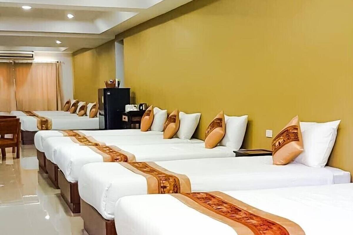 Ein Hotelzimmer mit mehreren Betten, die nebeneinander liegen, jeweils mit weißer Bettwäsche und braunen Kopfteilen.