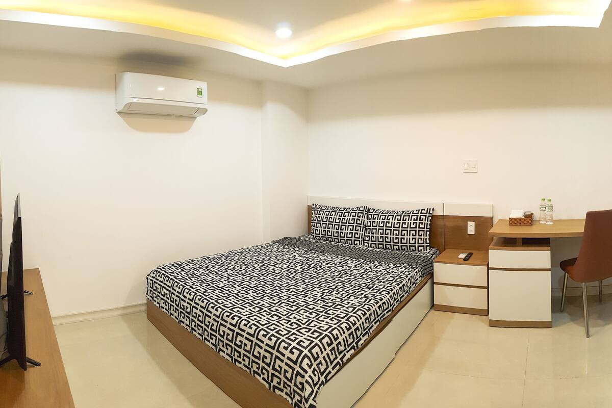 Quarto com cama, escrivaninha, cadeira, televisão e ar condicionado.