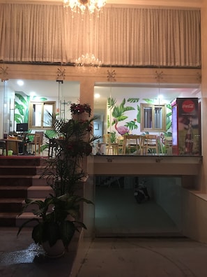 A hotel lobby with a staircase, a potted plant, a Coca-Cola refrigerator, and a wall with tropical wallpaper. - Tropical House (Ho Chi Minh City)