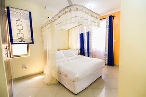 A bedroom with a four-poster bed, a window with a curtain, and a wall-mounted light fixture.