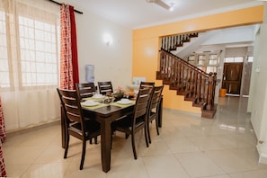 A dining area with a wooden table set for four, a staircase, and a kitchen in the background.