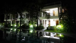 Un hotel moderno con piscina, rodeado de exuberante vegetación e iluminado con luz ambiental.