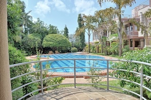 A swimming pool surrounded by lush greenery, with a metal railing in the foreground.