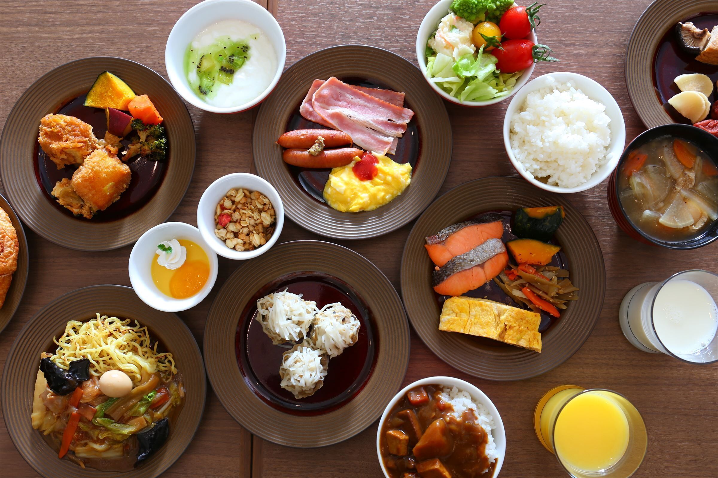 A variety of dishes on a wooden table, including rice, vegetables, and different types of meat.
