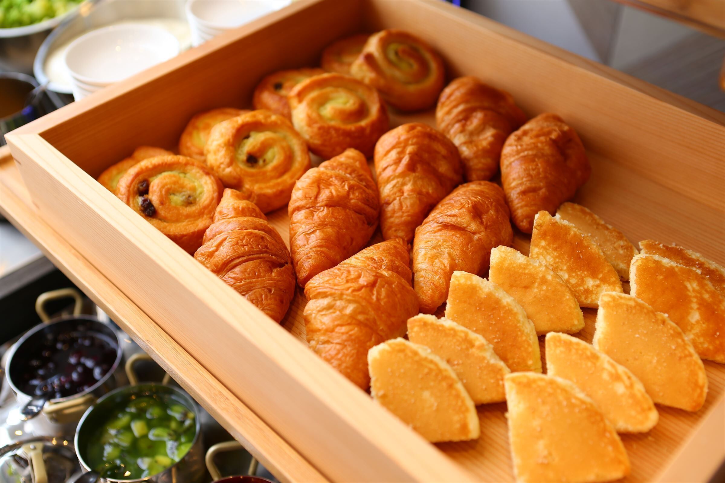 A wooden box containing various pastries and sliced bread.