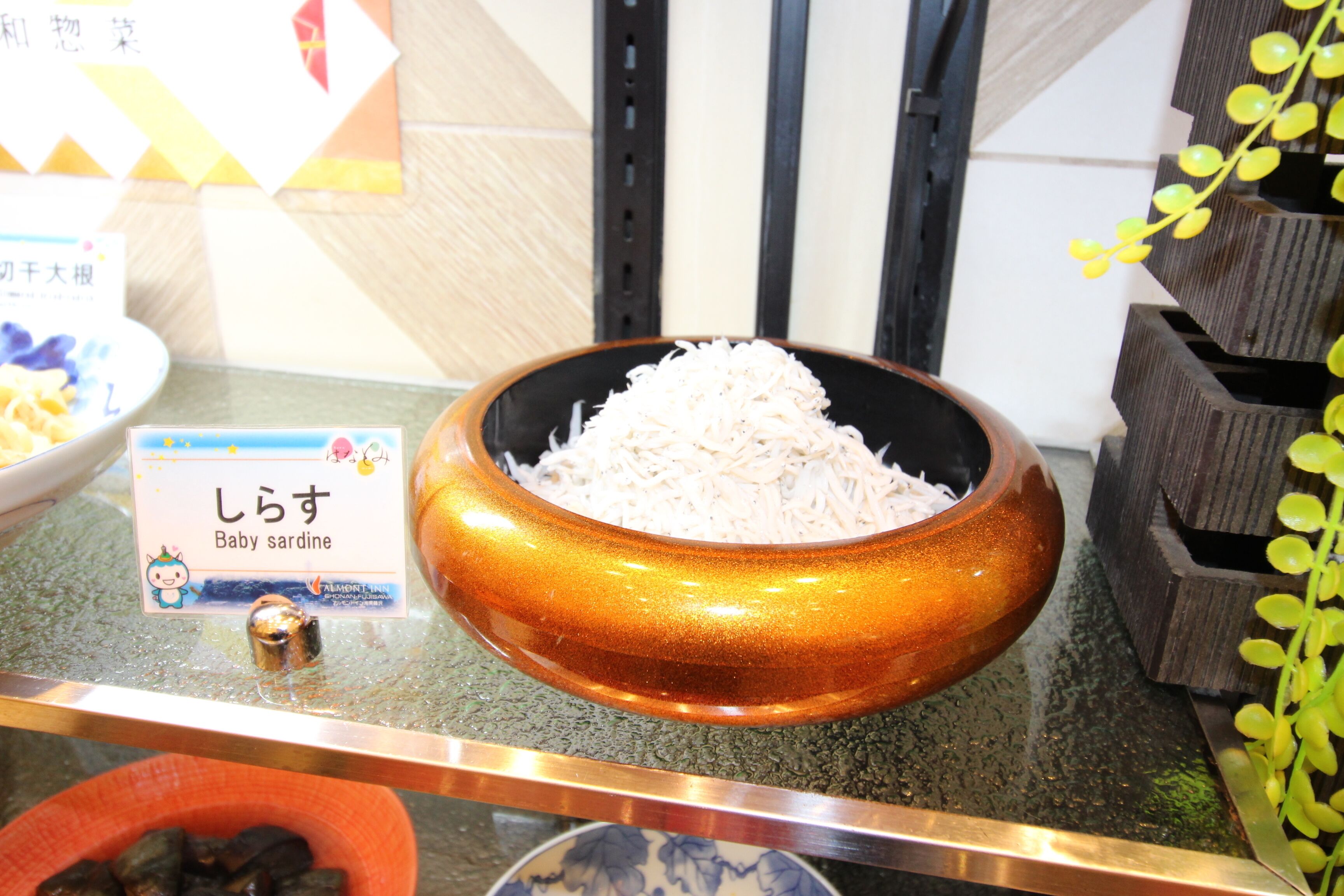 Un plato de sardinas bebé sobre una encimera con un cartel que dice "shirasu".