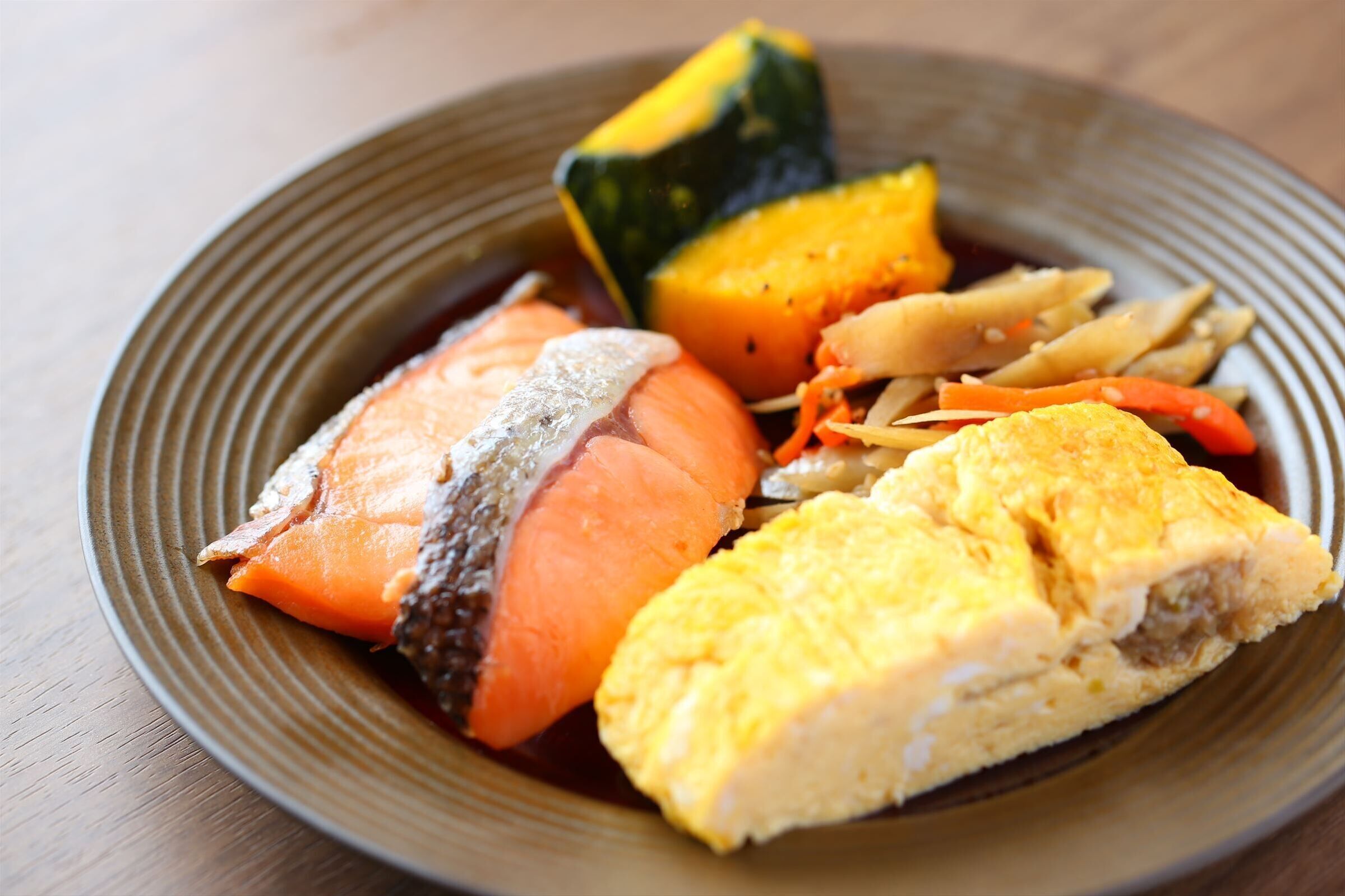 A plate with various foods including fish, vegetables, and a rolled omelette.