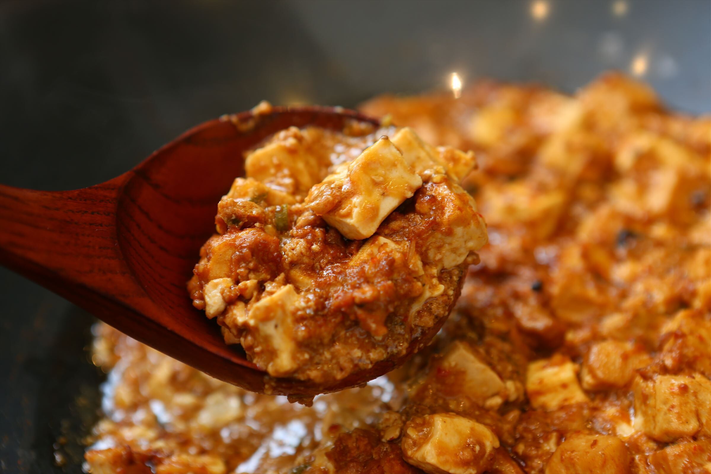 Una cuchara de madera sostiene una porción de guiso con trozos de carne y salsa.
