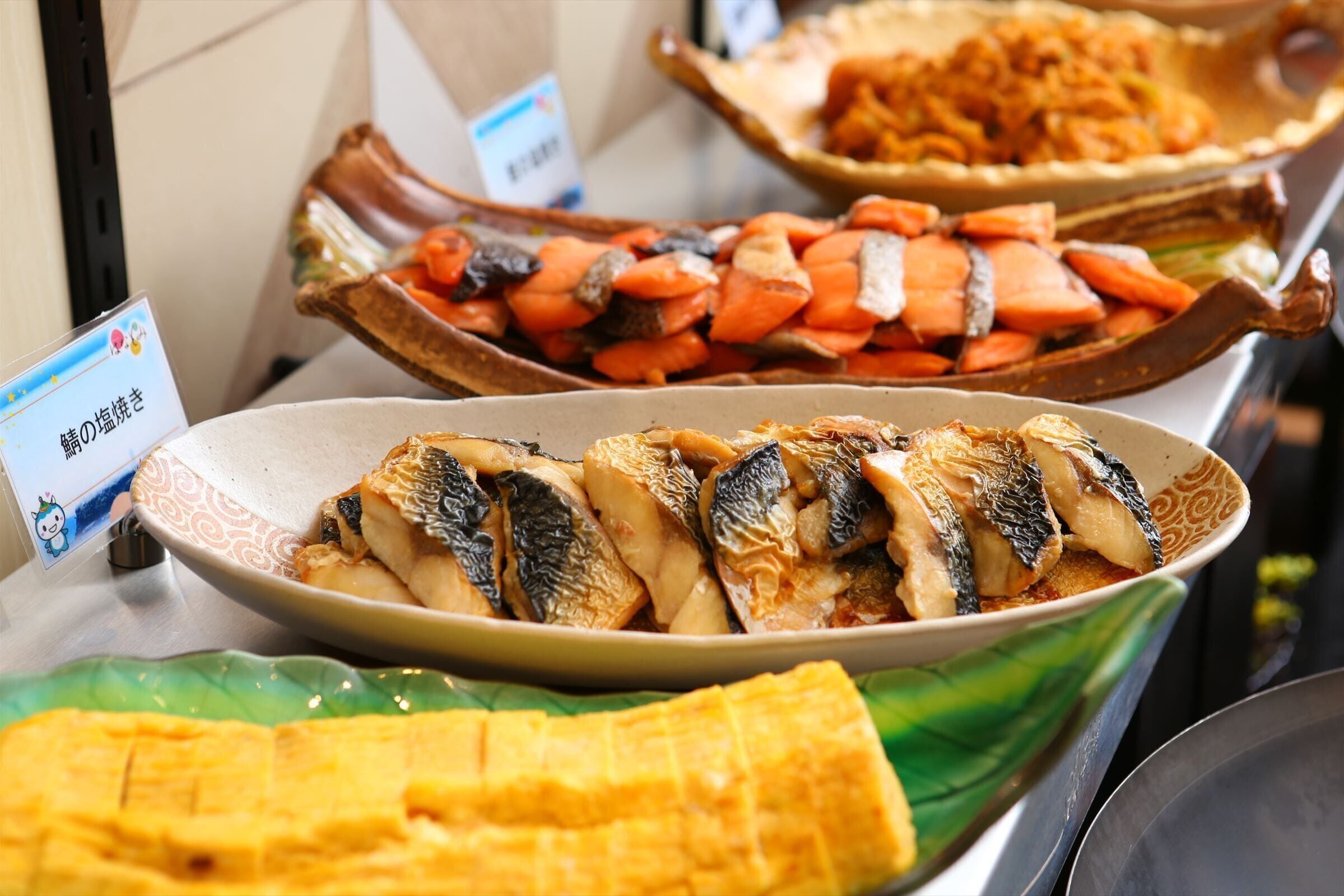 A buffet with various dishes including fish, vegetables, and a yellow dish.