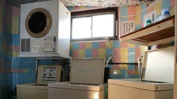 A laundry room with three washing machines, a window, and a colorful tiled wall.