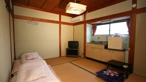 Een kleine, compacte kamer met een bed, een televisie, een kitchenette en een raam.