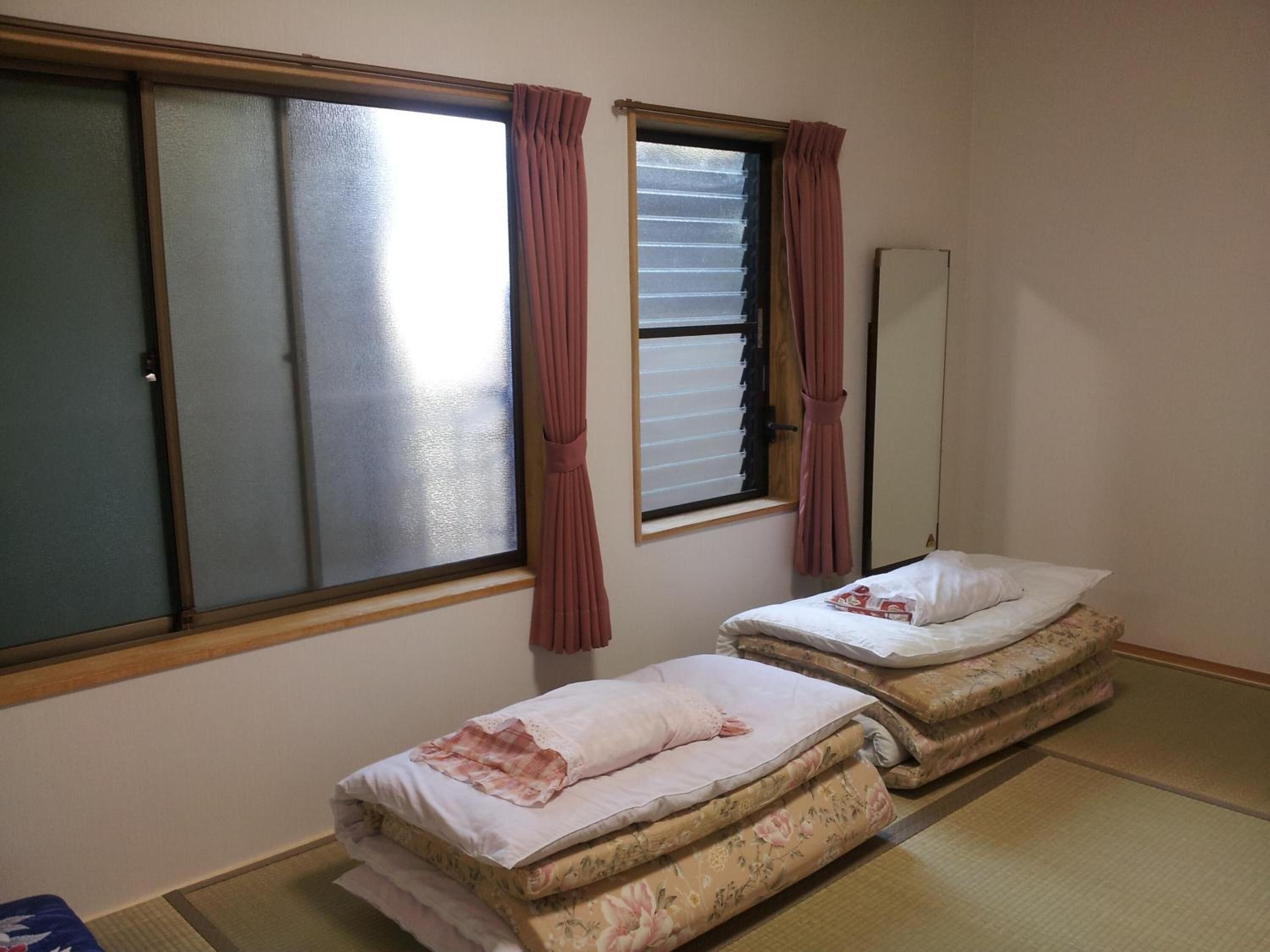 A room with two beds, a window with curtains, a mirror, and tatami flooring.