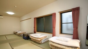 Een kamer met tatami matten, twee futons met kussens, een kleine tafel en een raam met gordijnen.