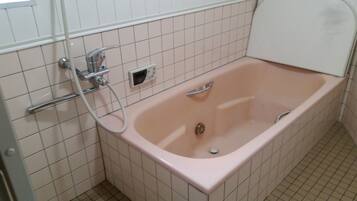 A bathroom with a pink bathtub, a handheld showerhead, and a wall-mounted control panel.