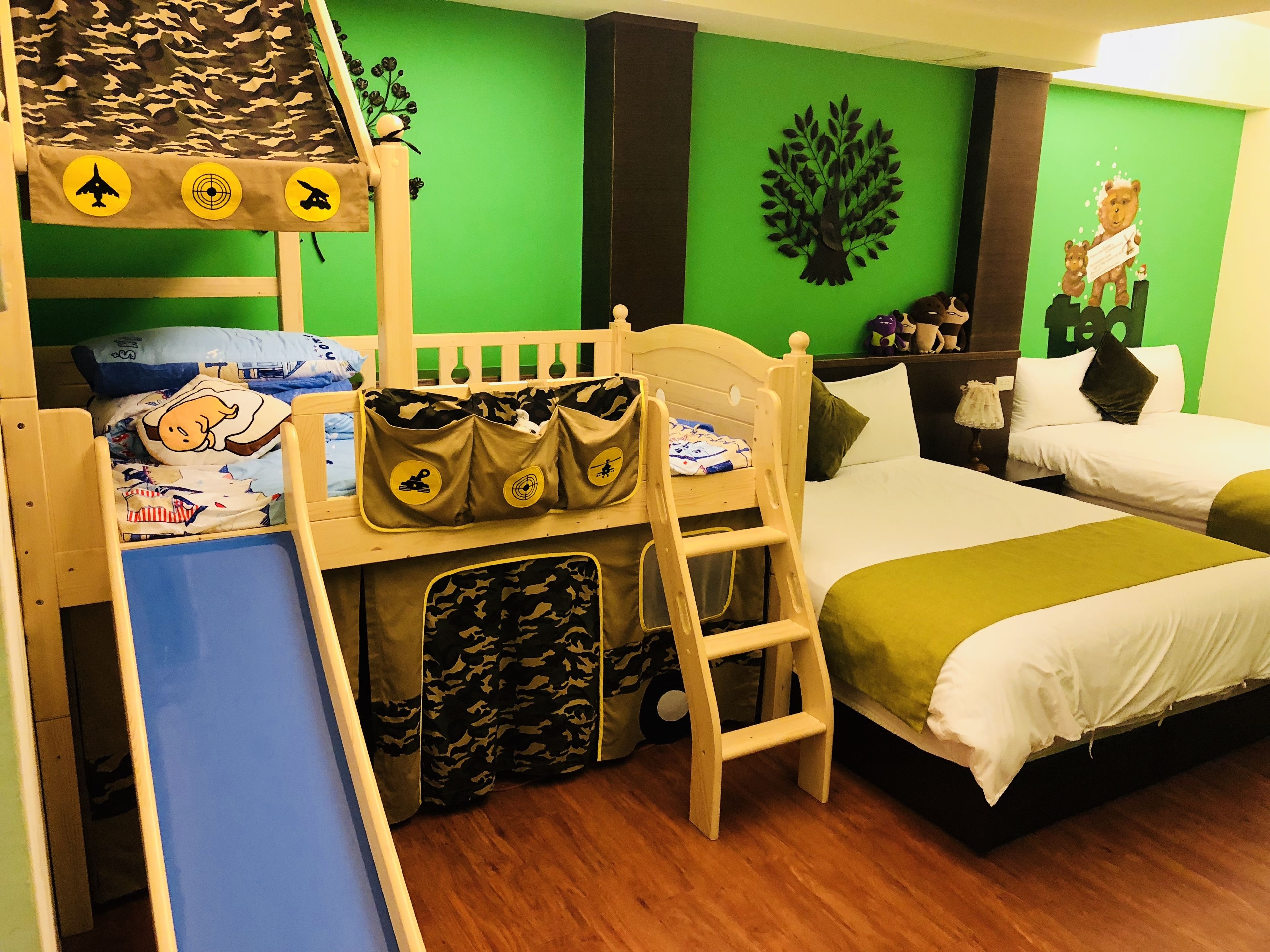 A bunk bed room with a slide, green walls, and a tree decoration.