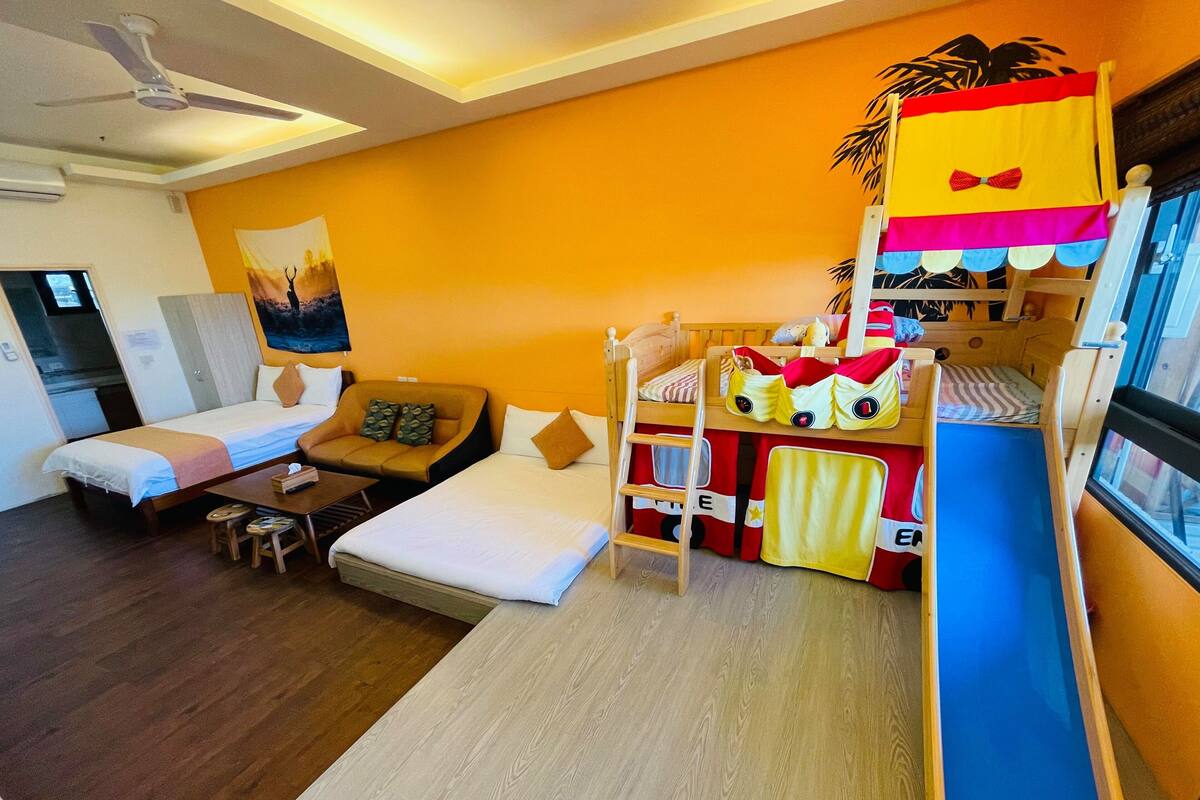 A hotel room with a bunk bed, a sofa bed, a desk, and a small table.
