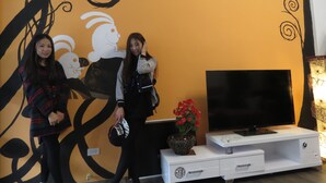 A room with a large TV on a white stand, a decorative wall with abstract designs, and a small table with a flower vase. - E-Phone hotel (Ji'an)