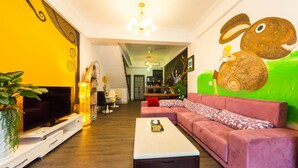 A living room with a TV, sofa, coffee table, and a green wall with a rabbit mural. - E-Phone hotel (Ji'an)