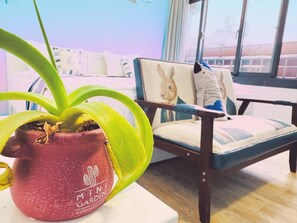 A potted plant on a table, a chair with a cushion, and a window with a view of buildings. - E-Phone hotel (Ji'an)