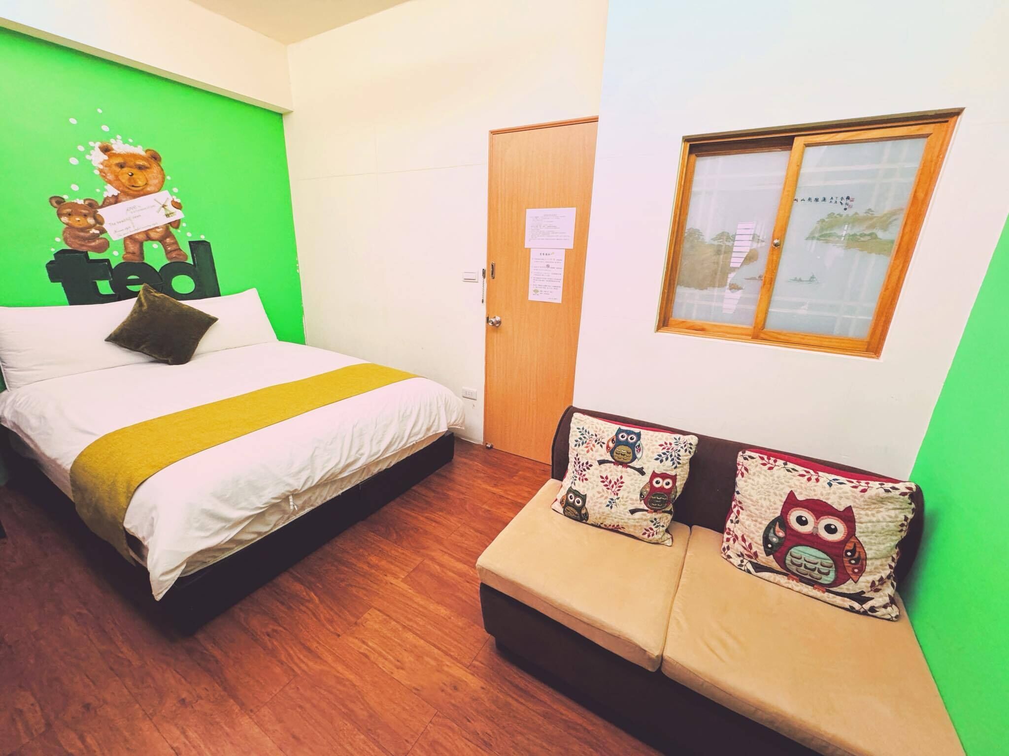 A room with a bed, a sofa, a green wall, a wooden door, and a window.