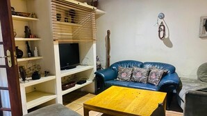 Ein Wohnzimmer mit einem blauen Sofa, einem Holztisch und einem Fernseher auf einem weißen Schrank.