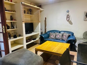 Ein Wohnzimmer mit einem blauen Sofa, einem Holztisch und einem Fernseher auf einem weißen Schrank.