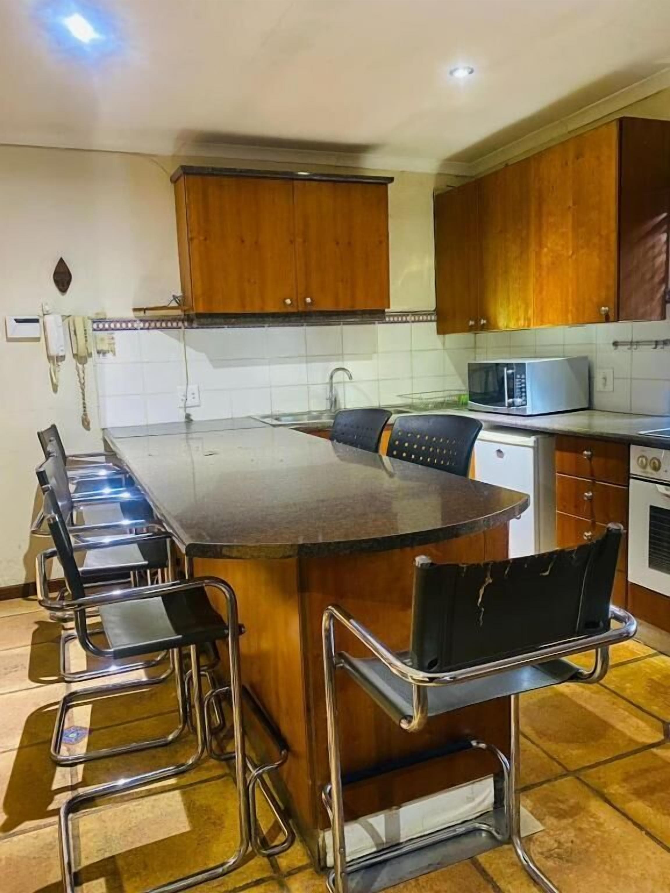 A kitchen with a central island, bar stools, a microwave, and wooden cabinets.