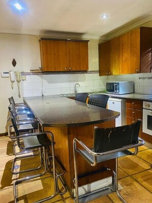 Une cuisine dotée d’un îlot central, de tabourets de bar, d’un four à micro-ondes et d’armoires en bois.