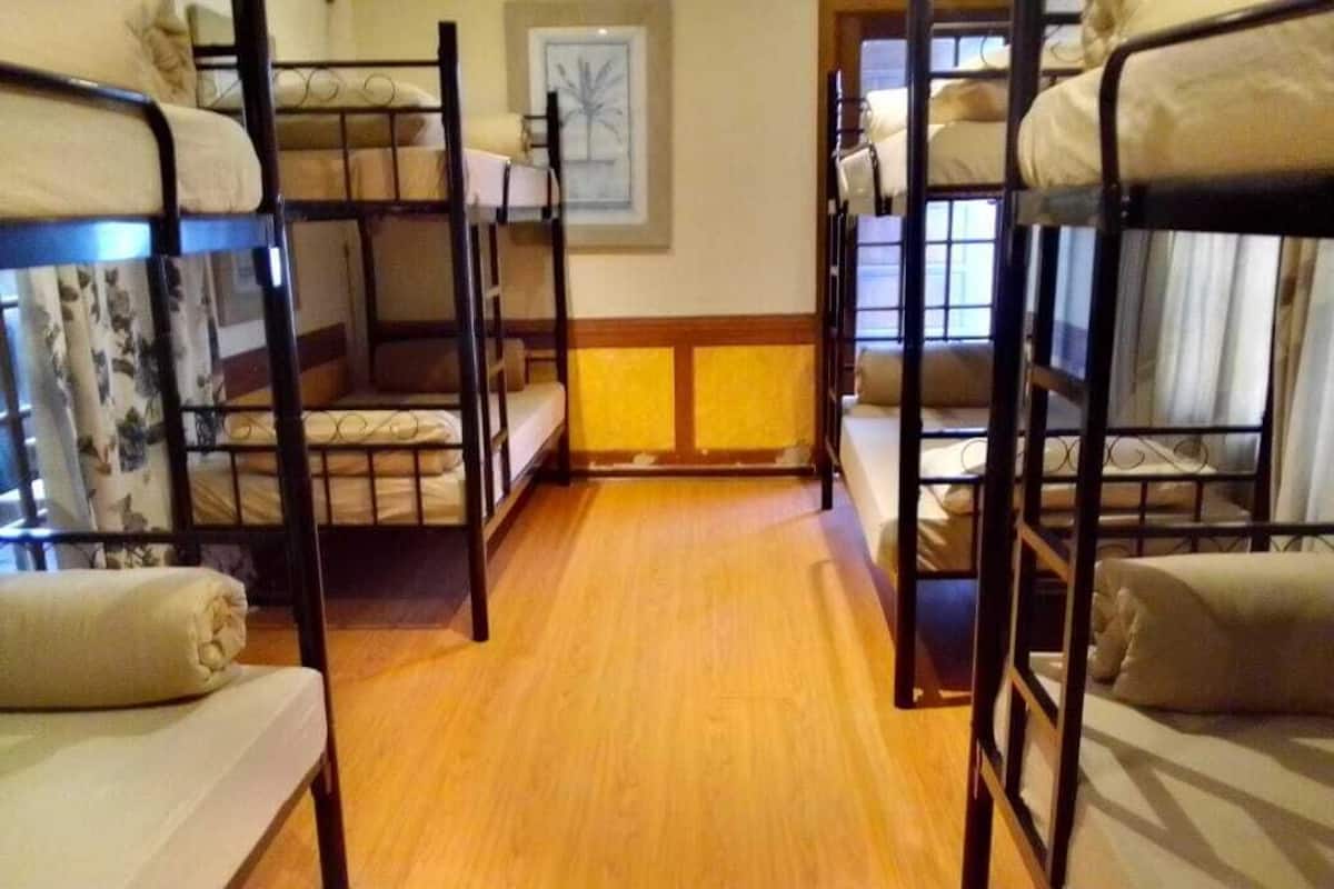Ein Zimmer mit Stockbetten, die paarweise auf einem Holzboden angeordnet sind, mit einem gerahmten Bild an der Wand.