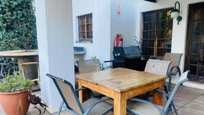 Eine Außenpatio mit Holztisch und Metallstühlen, einem Blumentopf und einem an der Wand befestigten Feuerlöscher.