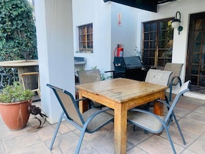 Eine Außenpatio mit Holztisch und Metallstühlen, einem Blumentopf und einem an der Wand befestigten Feuerlöscher.