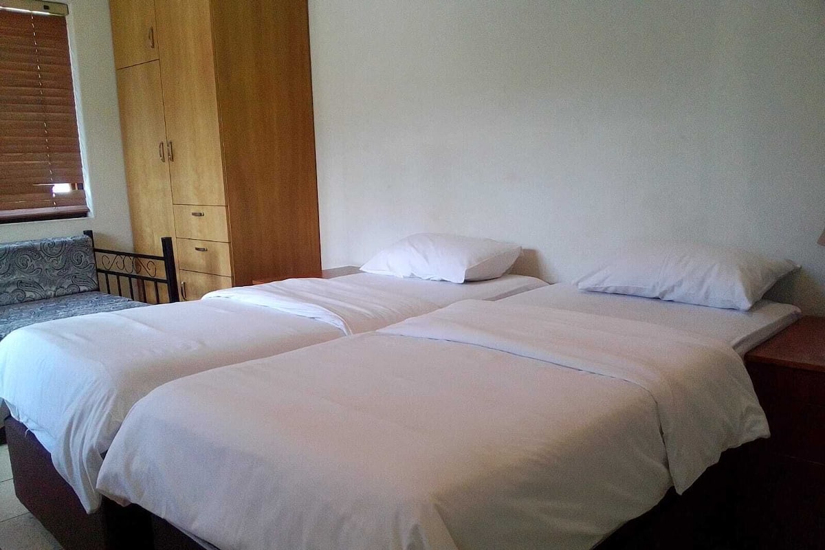 Ein Doppelbett mit weißer Bettwäsche in einem Zimmer mit Holzmöbeln und einem Fenster mit Jalousien.