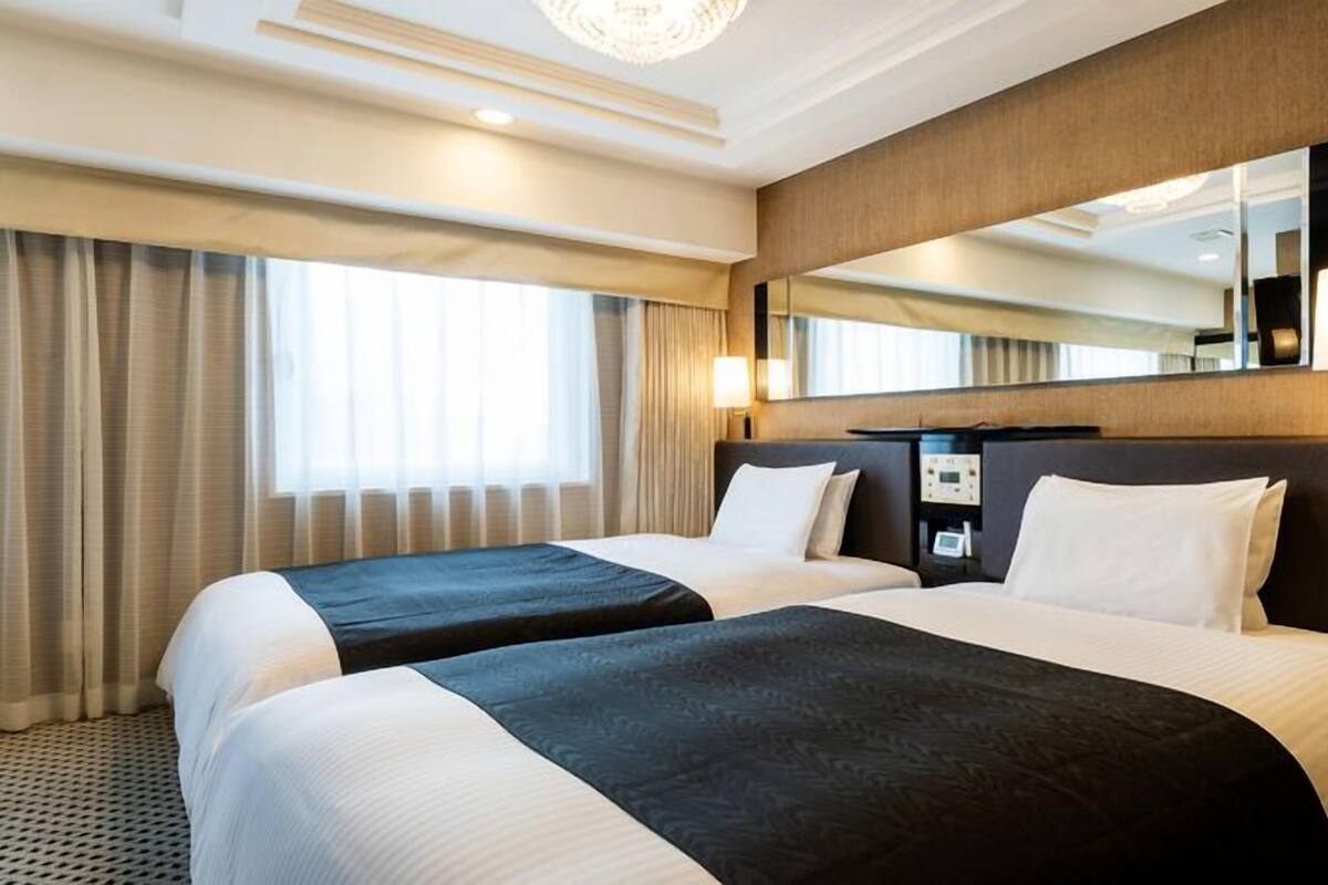 A hotel room with two beds, a large mirror, and a control panel.