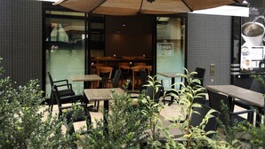Uma área de estar externa com mesas, cadeiras, um guarda-sol grande e uma máquina de café.