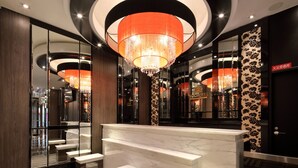 Um lobby de hotel moderno com um lustre imponente, balcão de recepção de mármore e um espelho refletindo o interior.