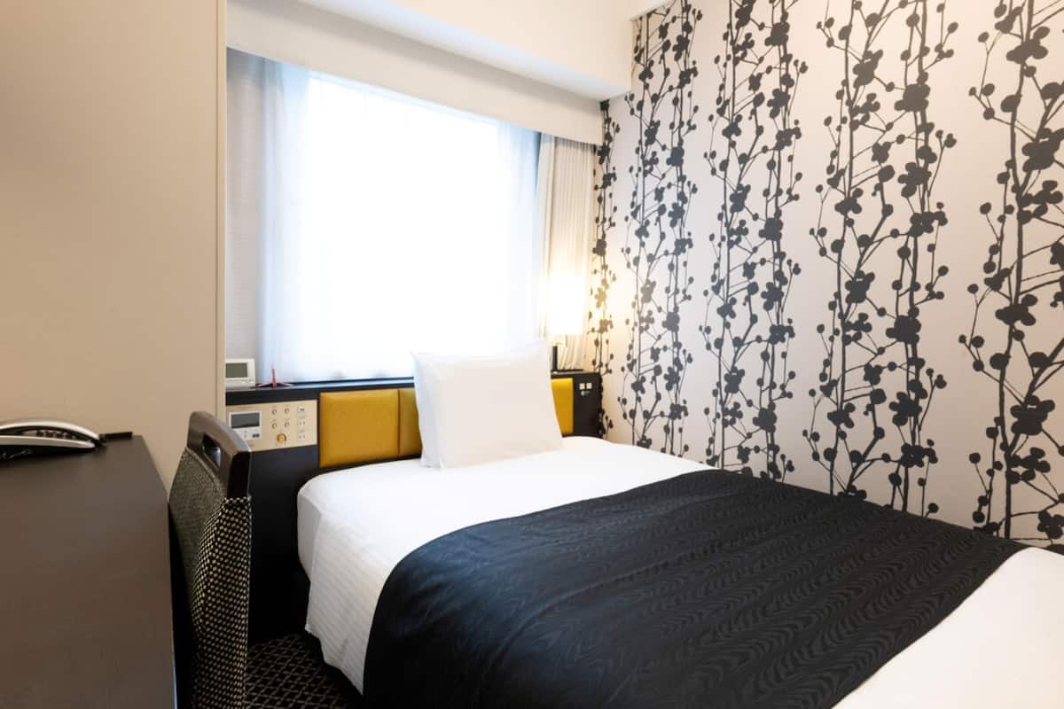 A hotel room with a bed, a bedside table, a lamp, and a window with curtains.