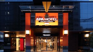 Exterior do APA HOTEL, com placa de identificação visível, entrada e edifícios modernos ao redor.