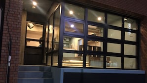 A modern building with a glass facade, a staircase leading to the entrance, and a visible interior with kitchen appliances. - hostel DEN (Tokyo)