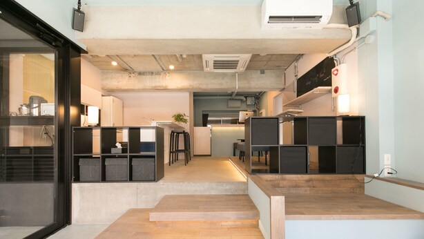 A modern kitchen with a central island, a dining area with stools, and a staircase leading to a second floor. - hostel DEN (Tokyo)