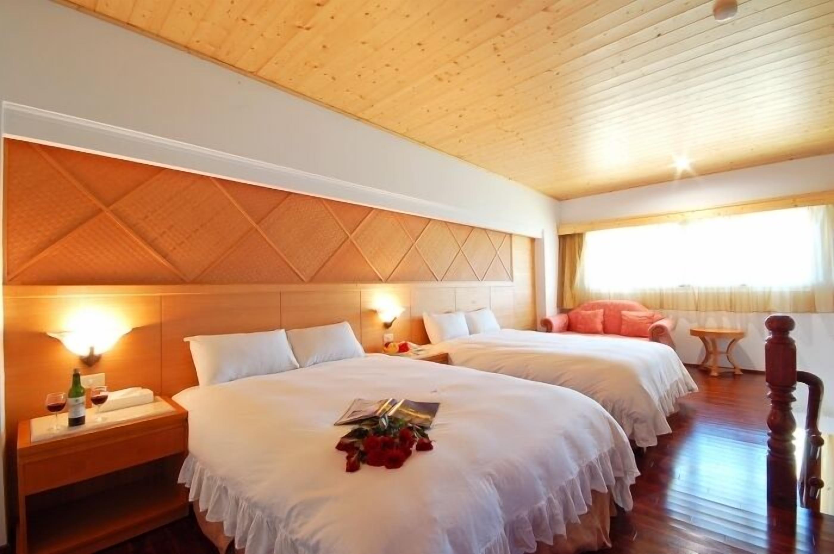 Una habitación de hotel con dos camas, cabeceros de madera, lámparas de noche y suelo de madera.