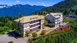 Un hotel de estilo chalete tradicional, con una estructura de dos pisos, una zona de estar al aire libre techada y vistas de las montañas circundantes.