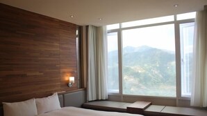 Una habitación de hotel con una cama grande, un panel de madera decorativo, una ventana con vistas a la montaña y una mesita de noche con lámpara.