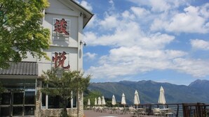 Un edificio con caracteres chinos, asientos exteriores con sombrillas y montañas al fondo.